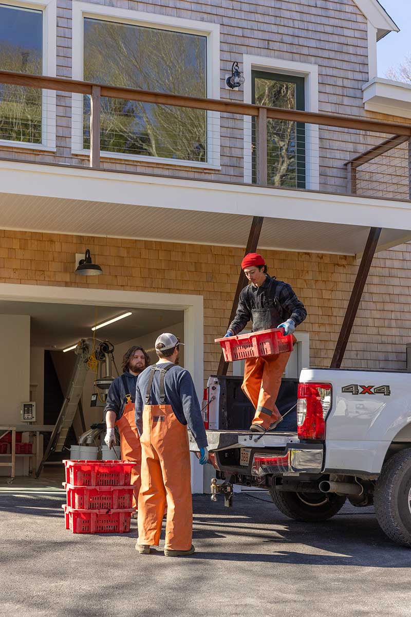 Workers hauling orange crates of oysters off a truck into the Deluxbury Sea Farm oyster processing facility.