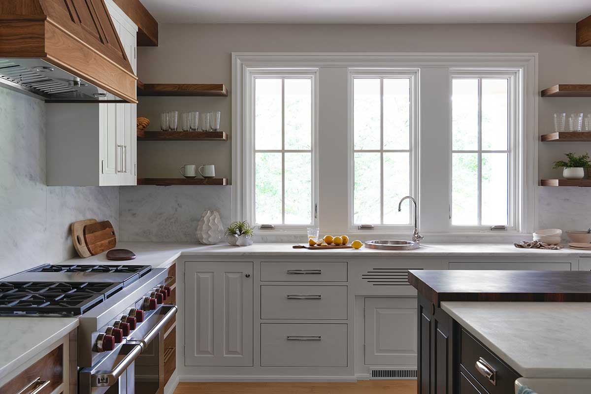 The kitchen in the Hadley House, with a large wooden hood above a gas range, large island and Marvin Ultimate Casement windows above the sink.