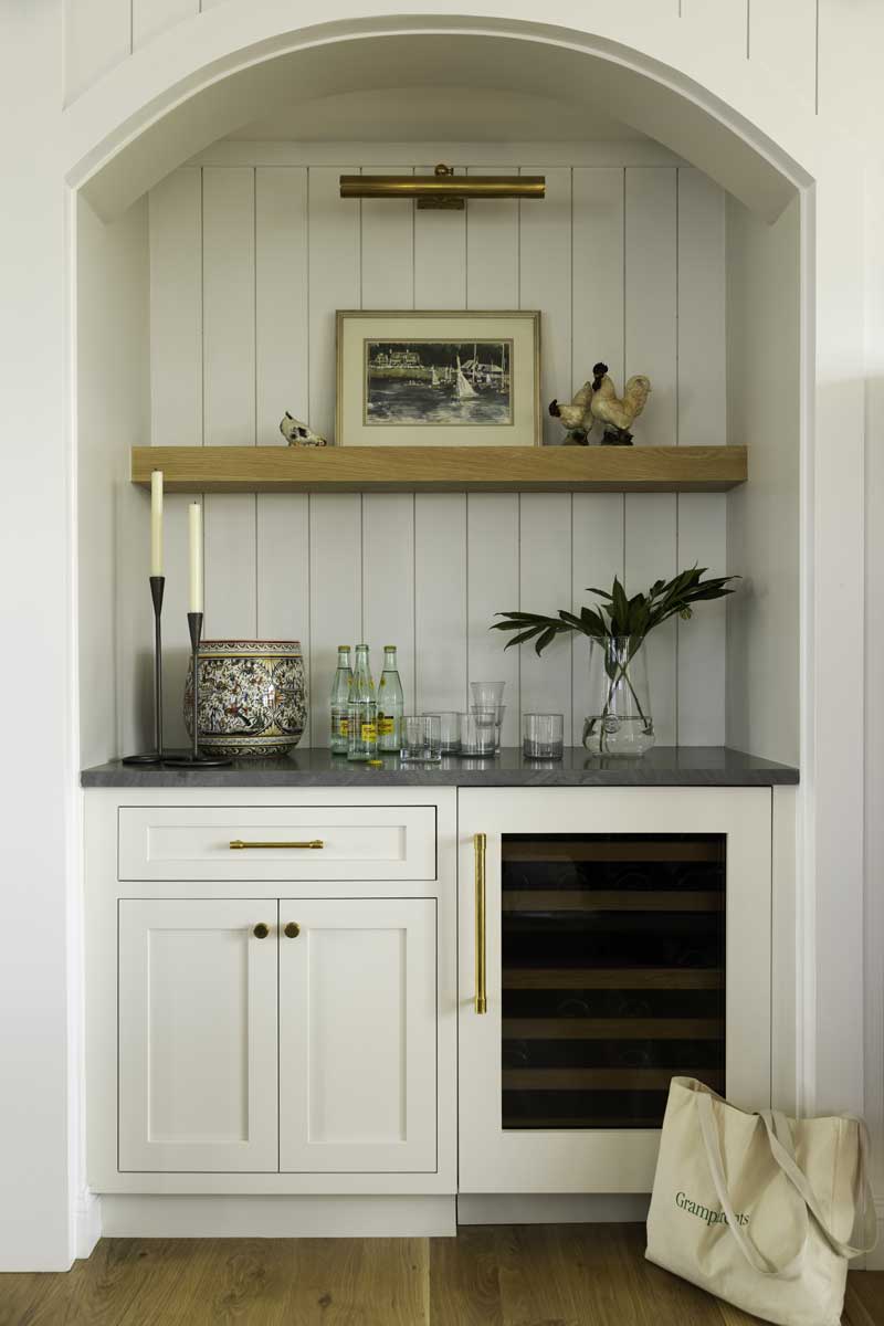 A built-in bar nook with wine cooler and cream cabinet with dark countertops and open shelving.