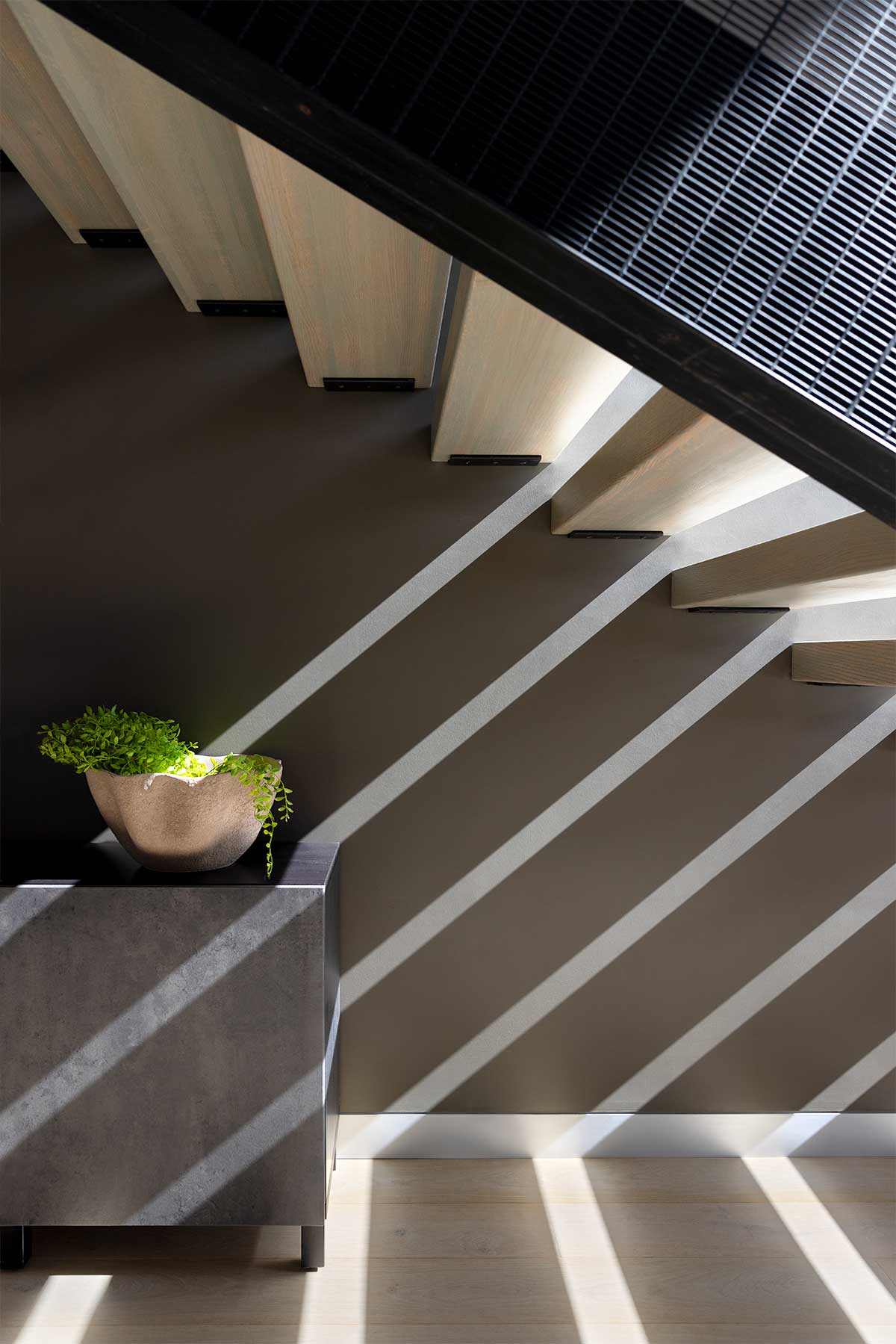 Light coming in through a modern staircase, casting shadows on a wall, through Marvin windows and a door.