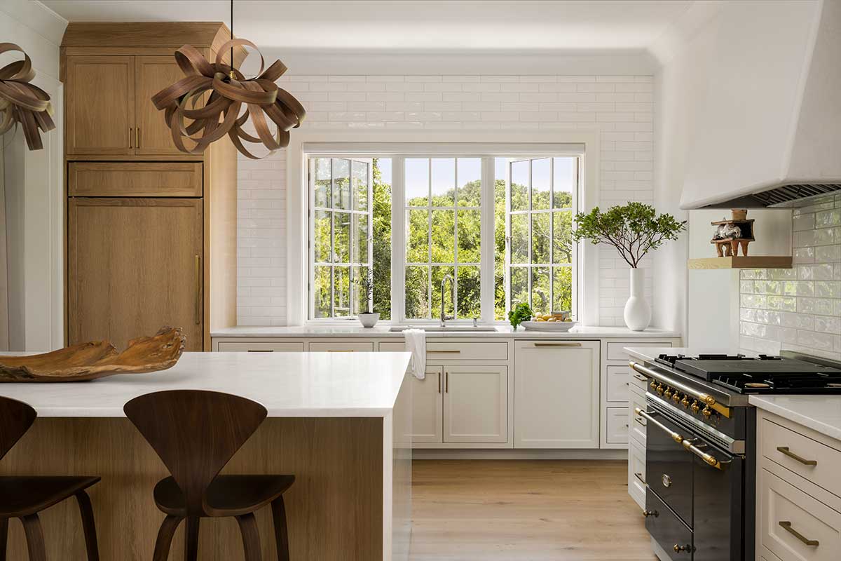 A kitchen with light wood and white cabinetry, black oven, and Marvin Ultimate Casement Push Out windows above the sink.